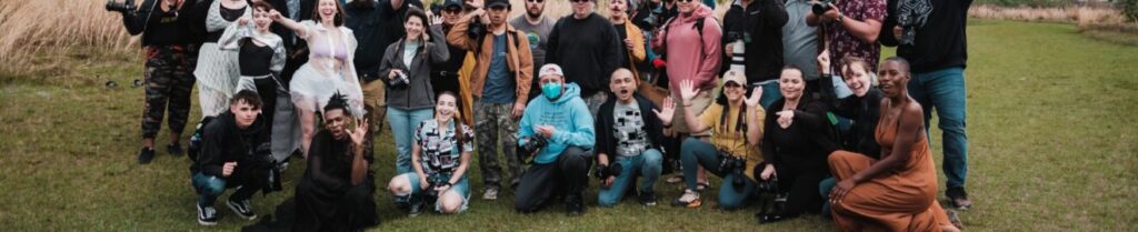 A diverse group of photographers posing together in a natural setting with cameras.